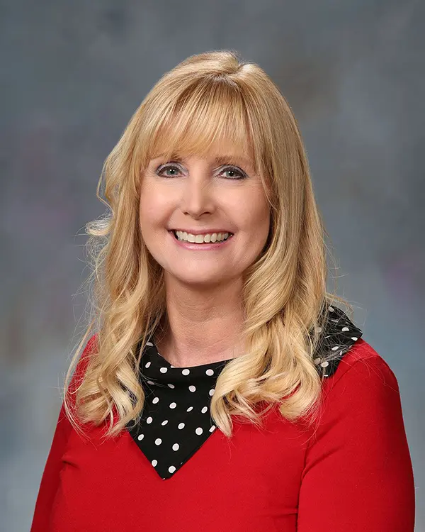 Portrait of a smiling woman with long blonde hair wearing a red blouse and a black polka dot scarf.